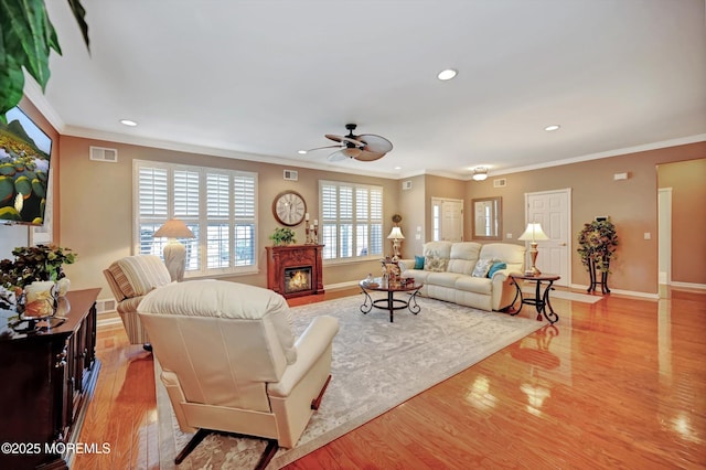 living room featuring light wood finished floors, a glass covered fireplace, visible vents, and baseboards