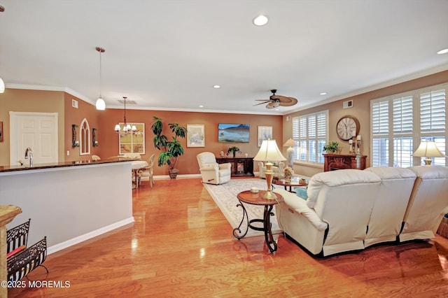 living room featuring recessed lighting, ornamental molding, light wood-style floors, baseboards, and ceiling fan with notable chandelier