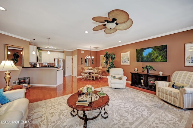 living area featuring light wood finished floors, ceiling fan with notable chandelier, ornamental molding, and recessed lighting