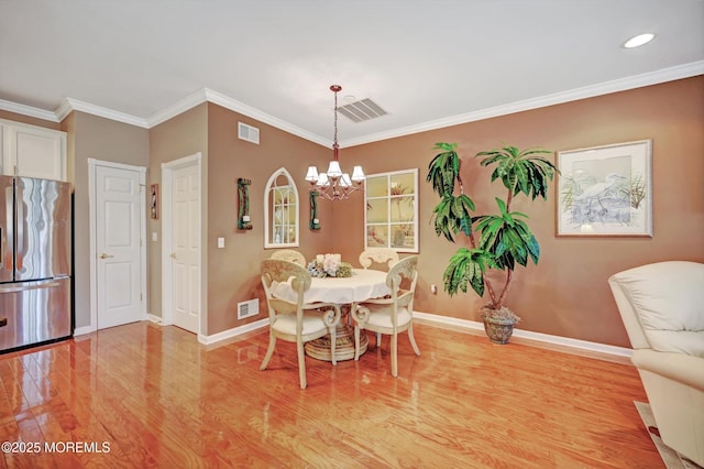 dining area with ornamental molding, light wood-type flooring, visible vents, and baseboards