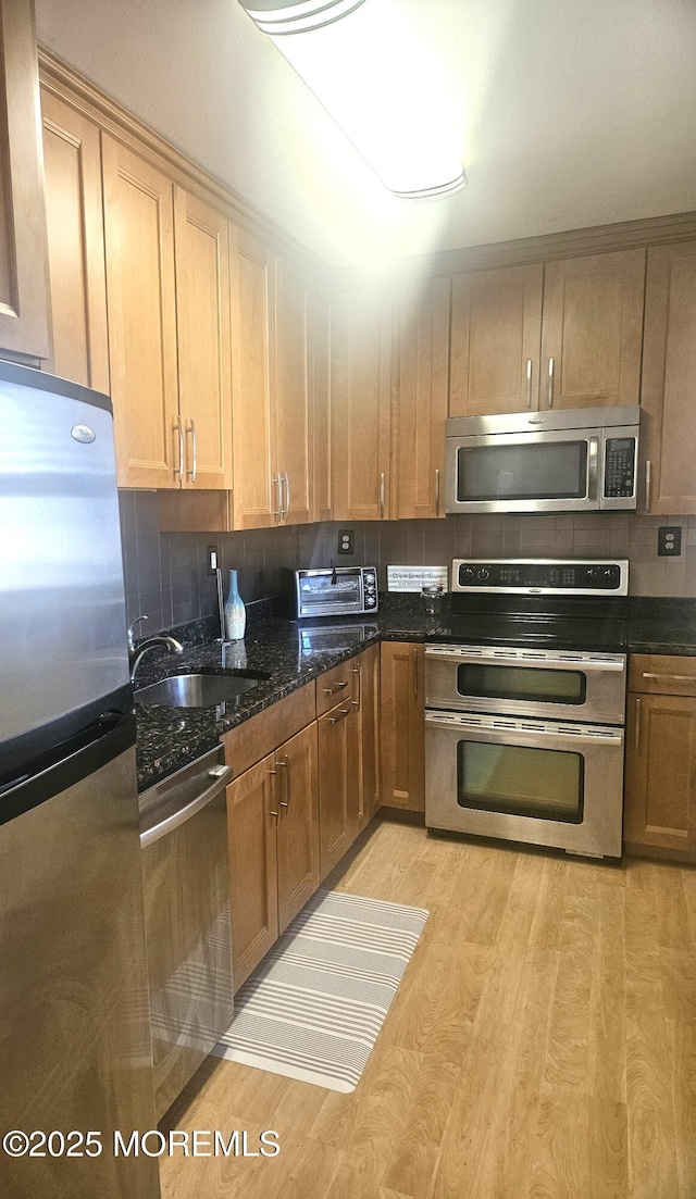 kitchen featuring light wood-type flooring, appliances with stainless steel finishes, decorative backsplash, and a sink