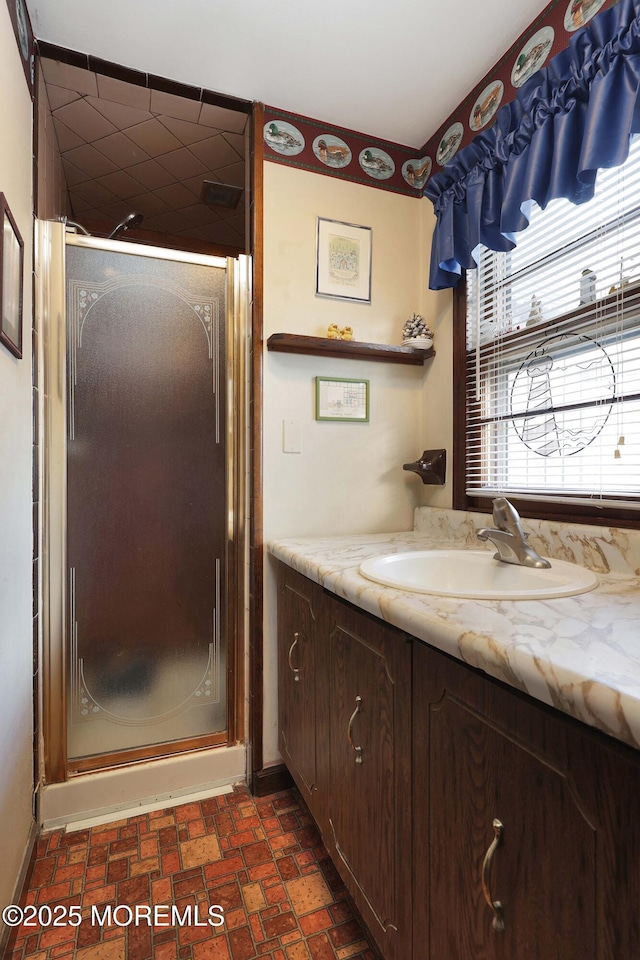 full bathroom with baseboards, a shower stall, vanity, and brick floor