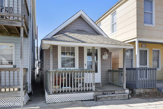 entrance to property featuring a porch and a shingled roof