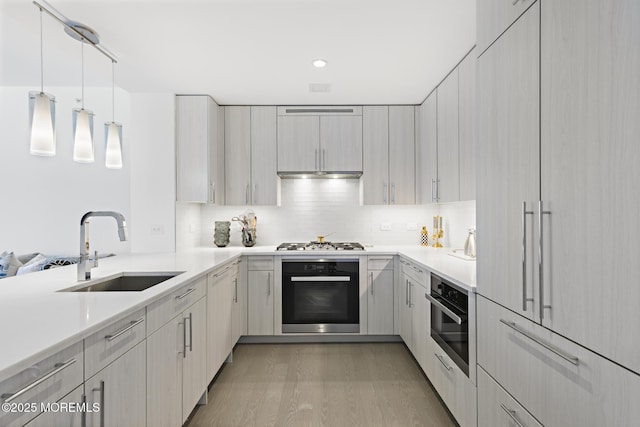 kitchen featuring light wood finished floors, a sink, stainless steel appliances, light countertops, and backsplash