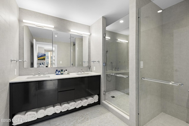 bathroom with a sink, tile walls, double vanity, and a shower stall