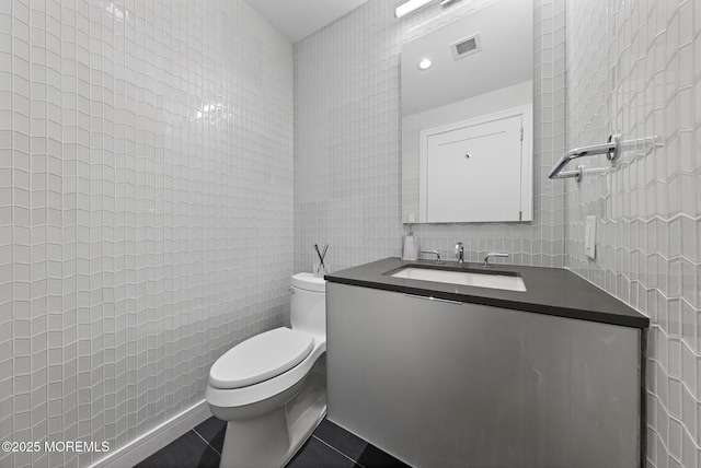 bathroom with tile patterned flooring, visible vents, toilet, vanity, and tile walls