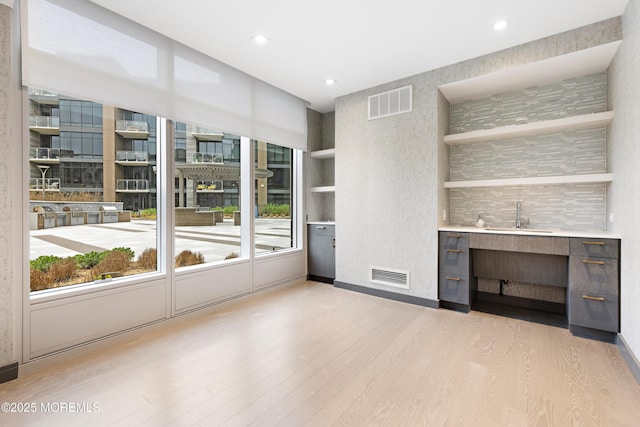 unfurnished living room with recessed lighting, visible vents, light wood-style flooring, and a sink