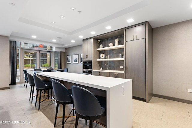 kitchen with a center island, a breakfast bar, light countertops, a raised ceiling, and open shelves