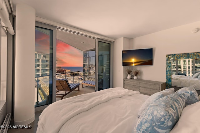 bedroom featuring access to exterior, baseboard heating, expansive windows, and wood finished floors