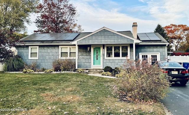 ranch-style home with roof mounted solar panels, a chimney, and a front lawn