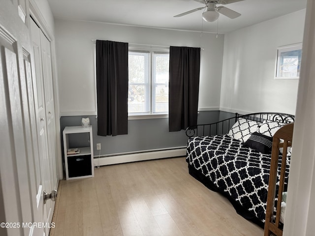 bedroom featuring a closet, a baseboard radiator, wood finished floors, and a ceiling fan