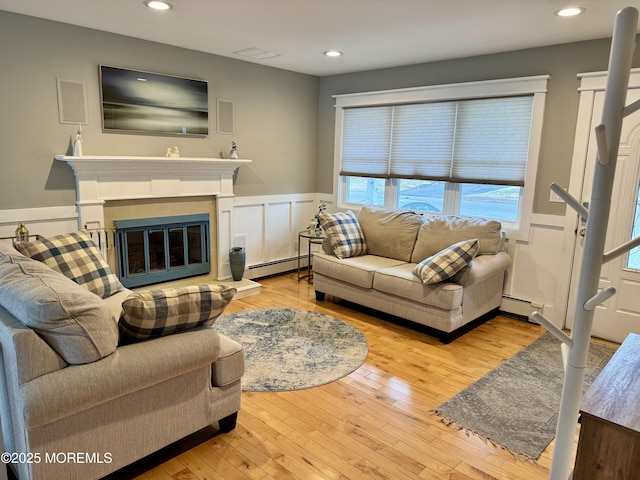 living room featuring a baseboard radiator, a wainscoted wall, a glass covered fireplace, and hardwood / wood-style floors