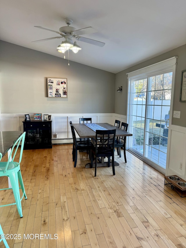 dining space featuring light wood-style floors, a baseboard heating unit, vaulted ceiling, and wainscoting