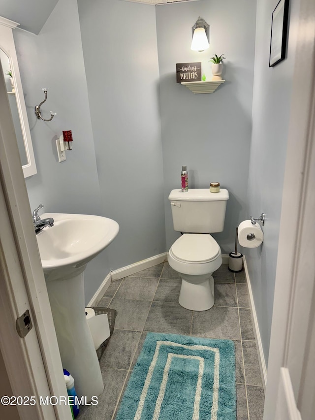 half bathroom with toilet, tile patterned flooring, baseboards, and a sink