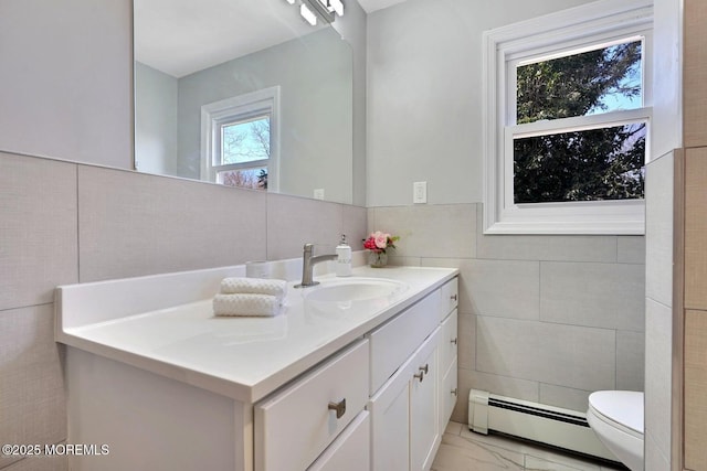 half bath with toilet, a baseboard heating unit, vanity, tile walls, and marble finish floor