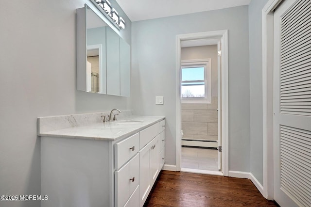 bathroom with a baseboard heating unit, vanity, baseboards, and wood finished floors