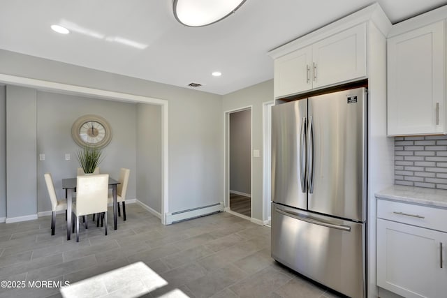 kitchen with visible vents, white cabinetry, baseboard heating, backsplash, and freestanding refrigerator