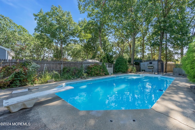 view of swimming pool featuring a fenced in pool, a fenced backyard, an outdoor structure, a shed, and a diving board