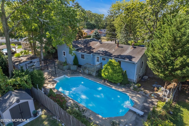 view of swimming pool featuring an outbuilding, a fenced backyard, a diving board, a fenced in pool, and a storage unit