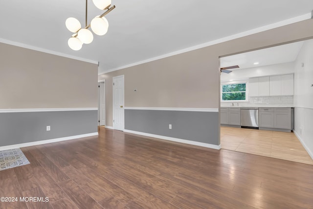 unfurnished living room featuring ceiling fan with notable chandelier, baseboards, wood finished floors, and ornamental molding