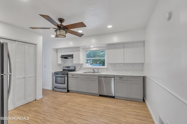 kitchen featuring under cabinet range hood, stainless steel appliances, a sink, light countertops, and gray cabinets