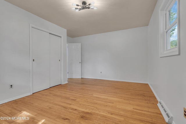 unfurnished bedroom featuring a closet, a baseboard radiator, light wood-style flooring, and baseboards