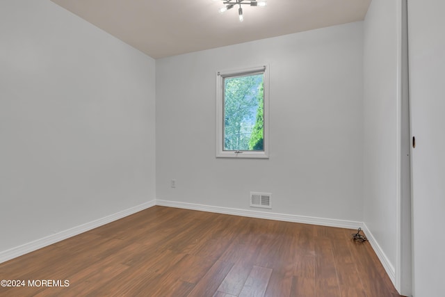 unfurnished room with dark wood-type flooring, visible vents, and baseboards