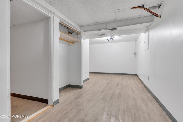 finished below grade area featuring light wood-type flooring, a paneled ceiling, and baseboards