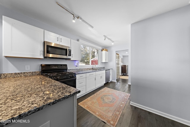 kitchen with white cabinets, dark wood finished floors, dark stone counters, appliances with stainless steel finishes, and a sink