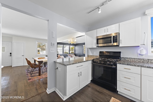 kitchen featuring a peninsula, dark wood-type flooring, gas stove, stainless steel microwave, and dark stone countertops