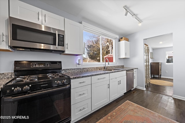 kitchen featuring stainless steel appliances, dark wood-style flooring, a sink, white cabinetry, and dark stone counters