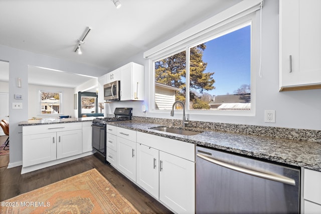 kitchen featuring stainless steel appliances, dark stone countertops, a sink, and white cabinets