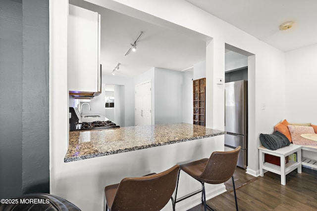 kitchen with dark wood-style flooring, freestanding refrigerator, white cabinetry, dark stone counters, and a peninsula