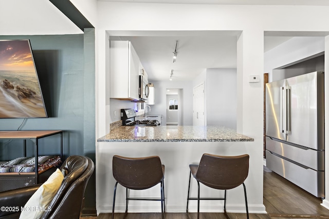 kitchen with dark wood finished floors, appliances with stainless steel finishes, a breakfast bar area, light stone countertops, and white cabinetry