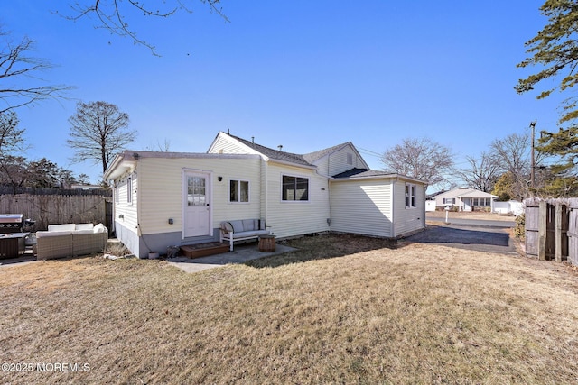 rear view of property with entry steps, outdoor lounge area, fence, and a lawn