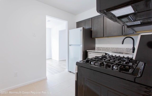 kitchen featuring range hood, a sink, light stone countertops, white appliances, and baseboards