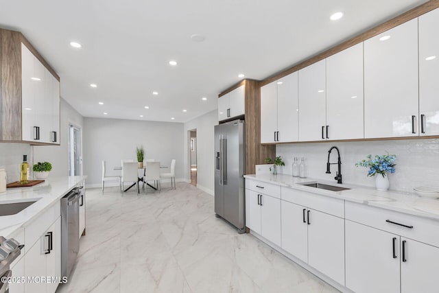 kitchen with appliances with stainless steel finishes, marble finish floor, a sink, and light stone countertops