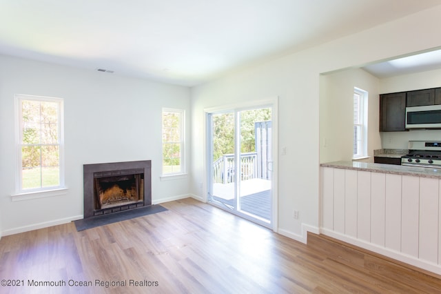 unfurnished living room featuring a fireplace with flush hearth, plenty of natural light, light wood-style flooring, and baseboards