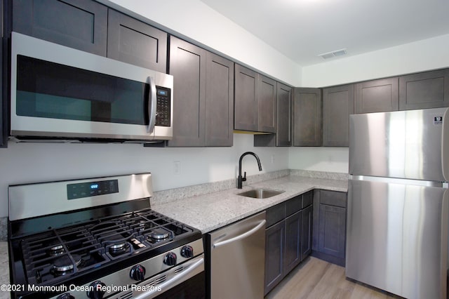 kitchen with light wood-style flooring, a sink, visible vents, appliances with stainless steel finishes, and light stone countertops