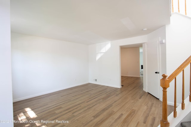 unfurnished room featuring wood finished floors, baseboards, and stairs