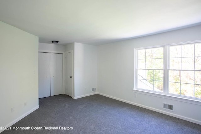 unfurnished bedroom with baseboards, visible vents, and dark carpet