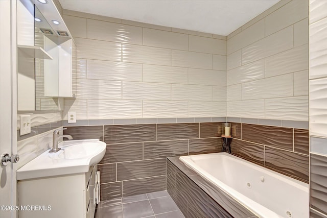 full bath featuring tile patterned flooring, tile walls, a tub with jets, and vanity