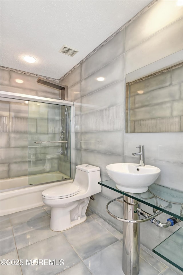 bathroom featuring visible vents, bath / shower combo with glass door, a sink, and toilet