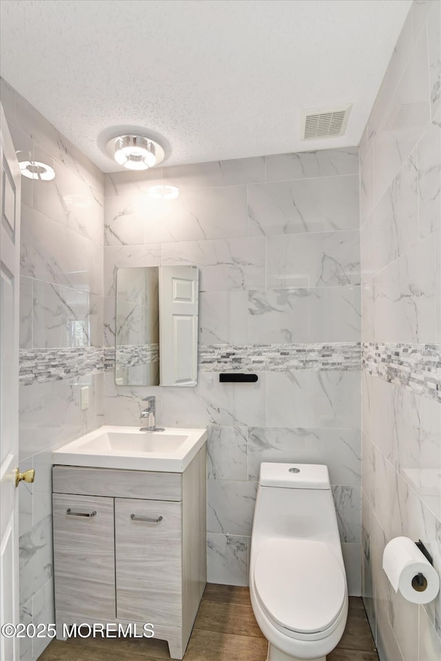 bathroom featuring visible vents, toilet, wood finished floors, a textured ceiling, and vanity