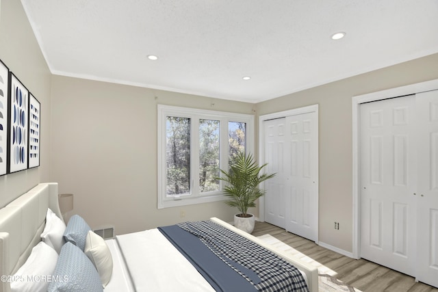 bedroom with baseboards, light wood finished floors, recessed lighting, and multiple closets