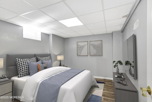 bedroom featuring a drop ceiling, baseboards, and wood finished floors