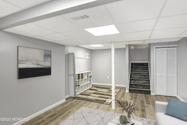 finished basement featuring stairway, visible vents, a drop ceiling, and wood finished floors