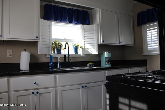 kitchen with dark countertops, a healthy amount of sunlight, a sink, and white cabinetry