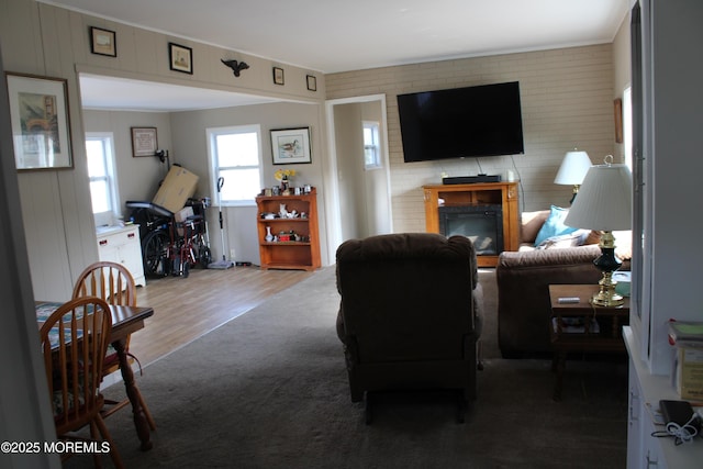 living room featuring crown molding, a glass covered fireplace, carpet flooring, brick wall, and wood finished floors