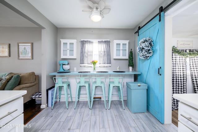 kitchen with light countertops, a barn door, glass insert cabinets, wood tiled floor, and white cabinets